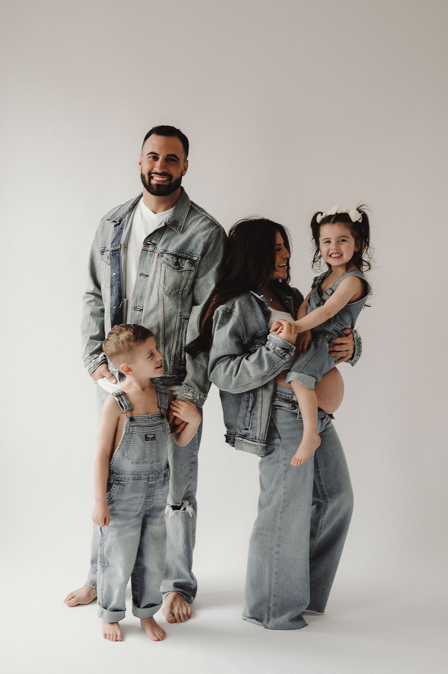 Family wearing coordinated denim outfits poses against white studio background.