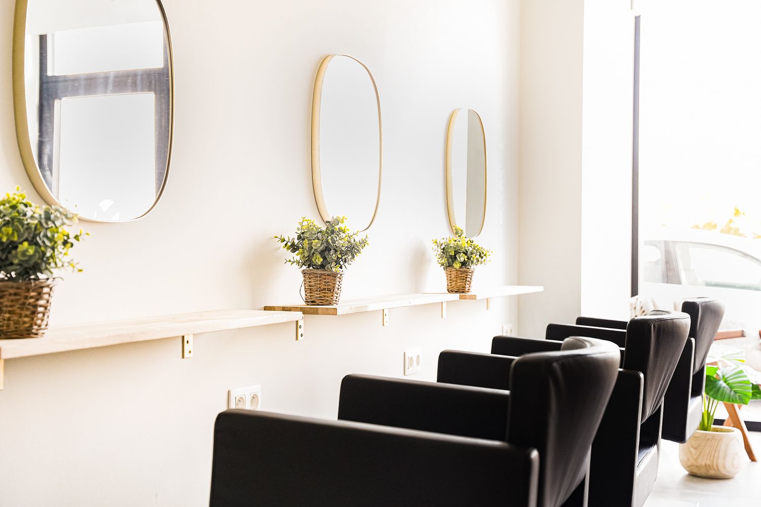 Modern salon interior with black chairs and gold-framed mirrors along white wall.