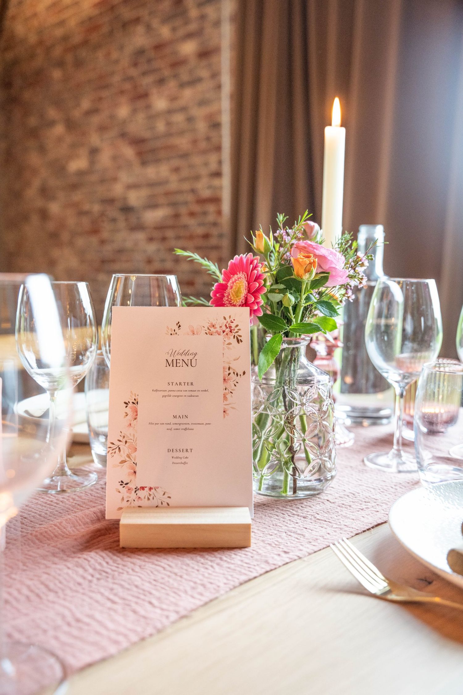 Elegant table setting with pink menu card, floral centerpiece, and white taper candle.