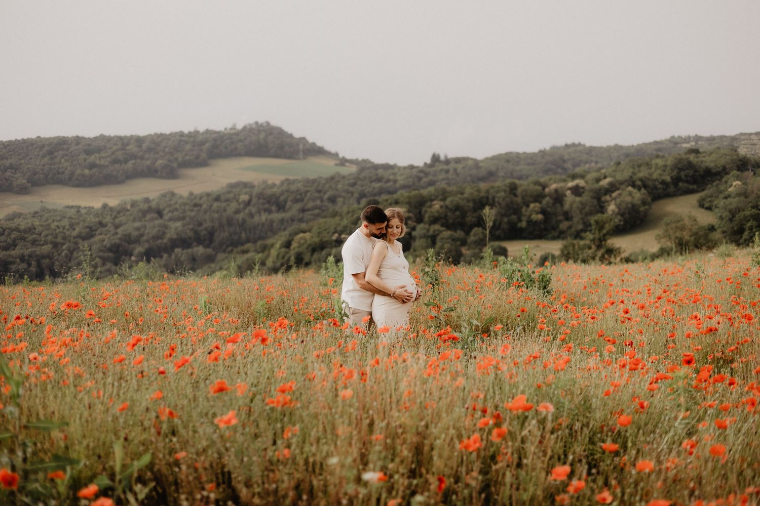 Photo d'un couple dans un champ de coquelicot pour une séance photo grossesse. Ils s'enlacent.