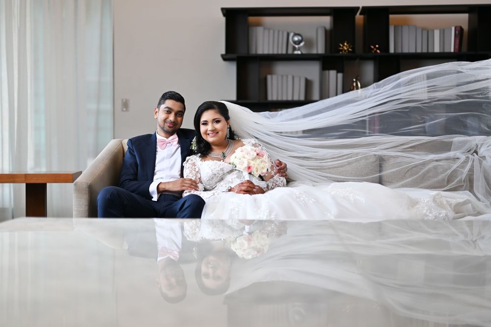 Couple poses with flowing veil in elegant indoor setting with bookshelves.