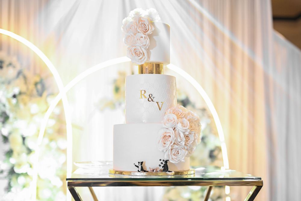 Elegant white wedding cake with delicate floral details displayed on gold stand.
