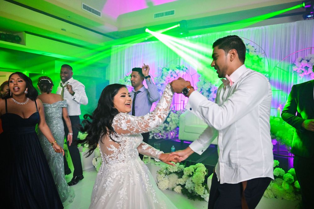 Couple energetically dancing at wedding reception under vibrant green lighting.