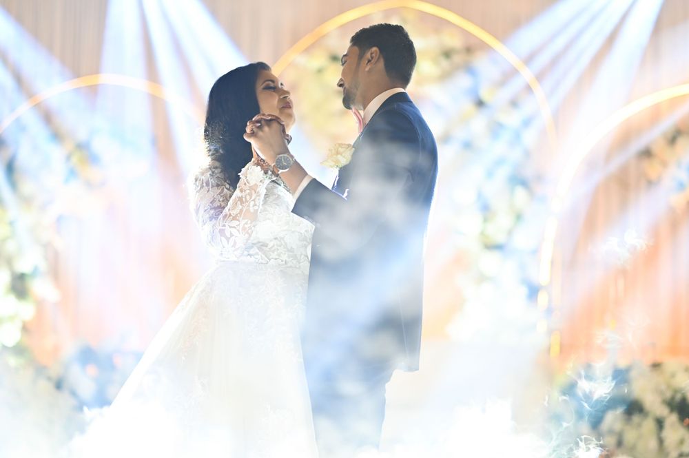 Newlywed couple sharing an intimate moment during their first dance surrounded by dramatic lighting and fog effects.