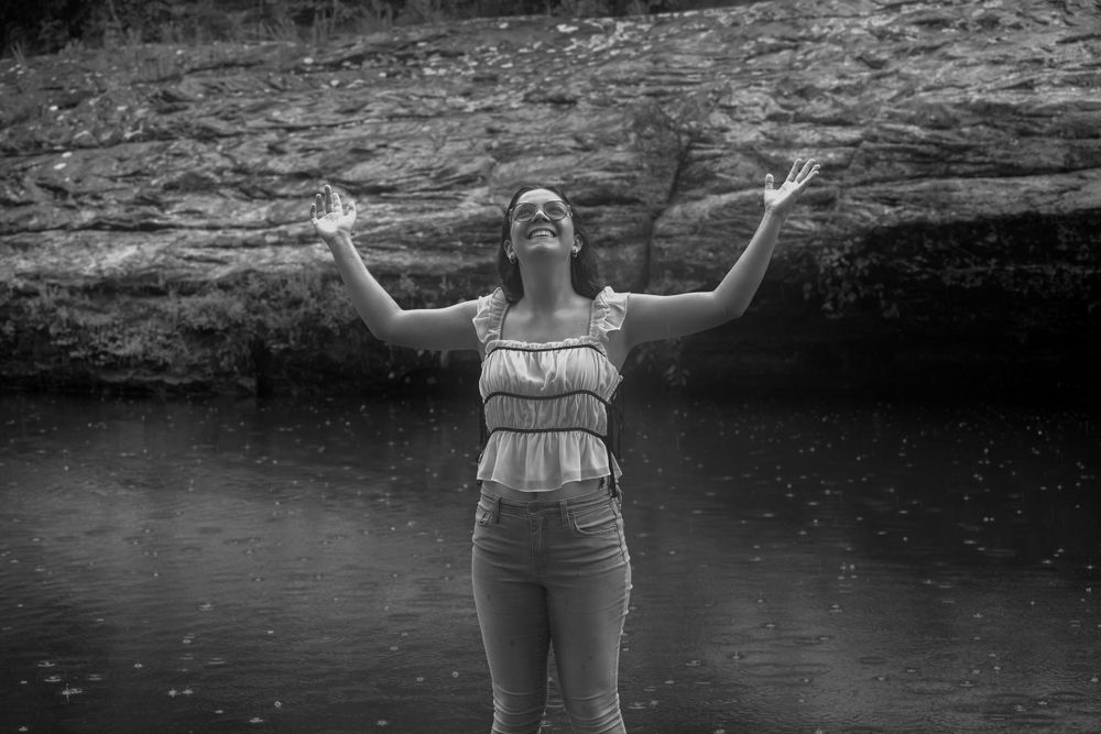 A black and white capture of joy with arms raised by the water.
