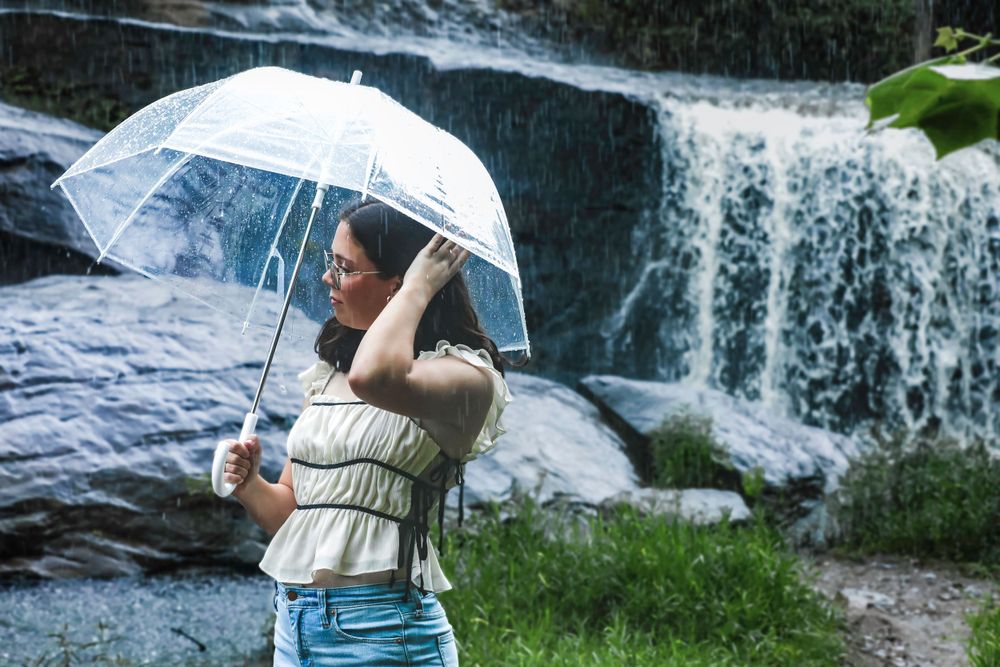 A clear umbrella provides shelter while viewing a scenic waterfall.