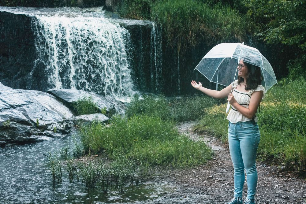 A serene moment by the waterfall holding a clear umbrella on a rainy day.