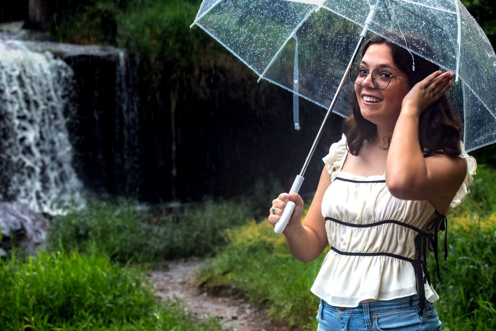 A clear umbrella frames a waterfall scene in a lush green forest setting.