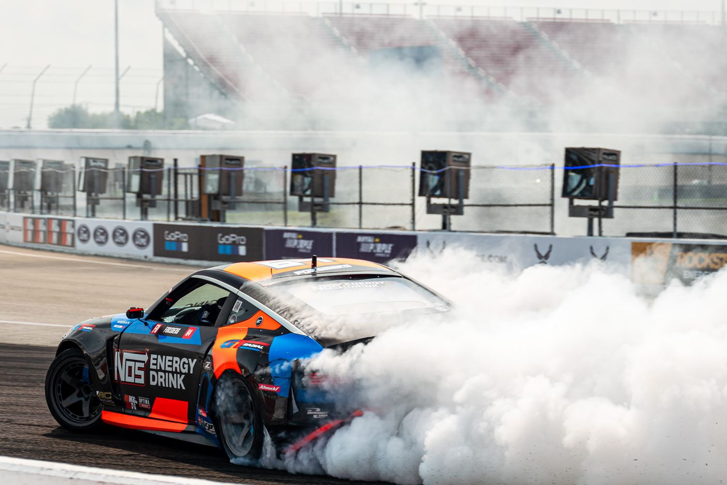Race car performing a dramatic burnout with thick white tire smoke at a race track.