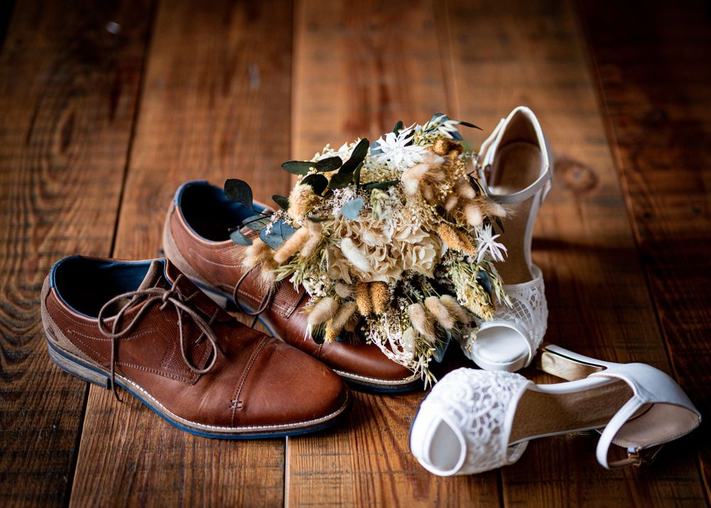 Wedding shoes arranged on rustic wooden flooring with dress details.