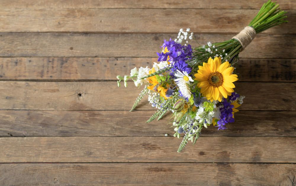 A rustic wedding bouquet with sunflowers and purple flowers on wooden background.