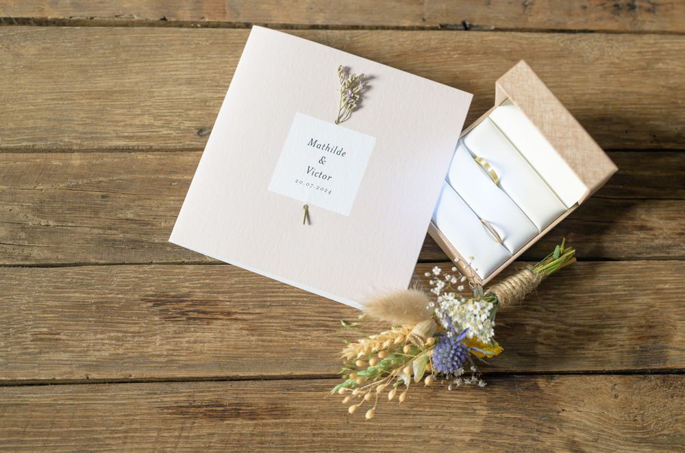 Wedding stationery and dried flowers arranged on rustic wooden table.