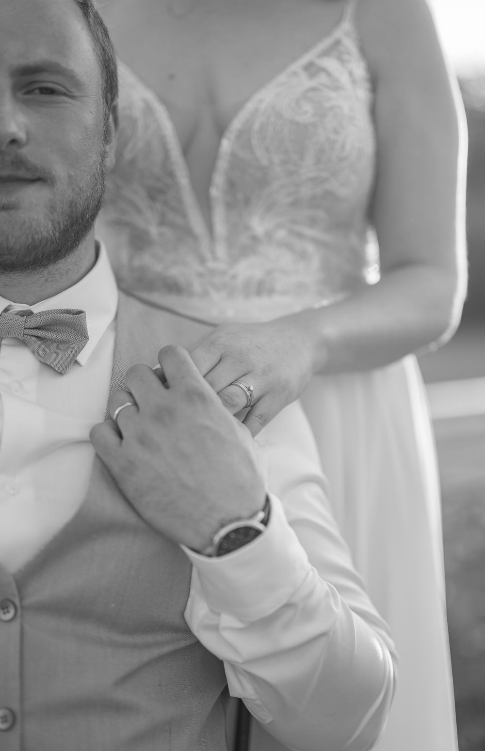 Black and white wedding photo showing close-up details of groom adjusting his tie and suit.