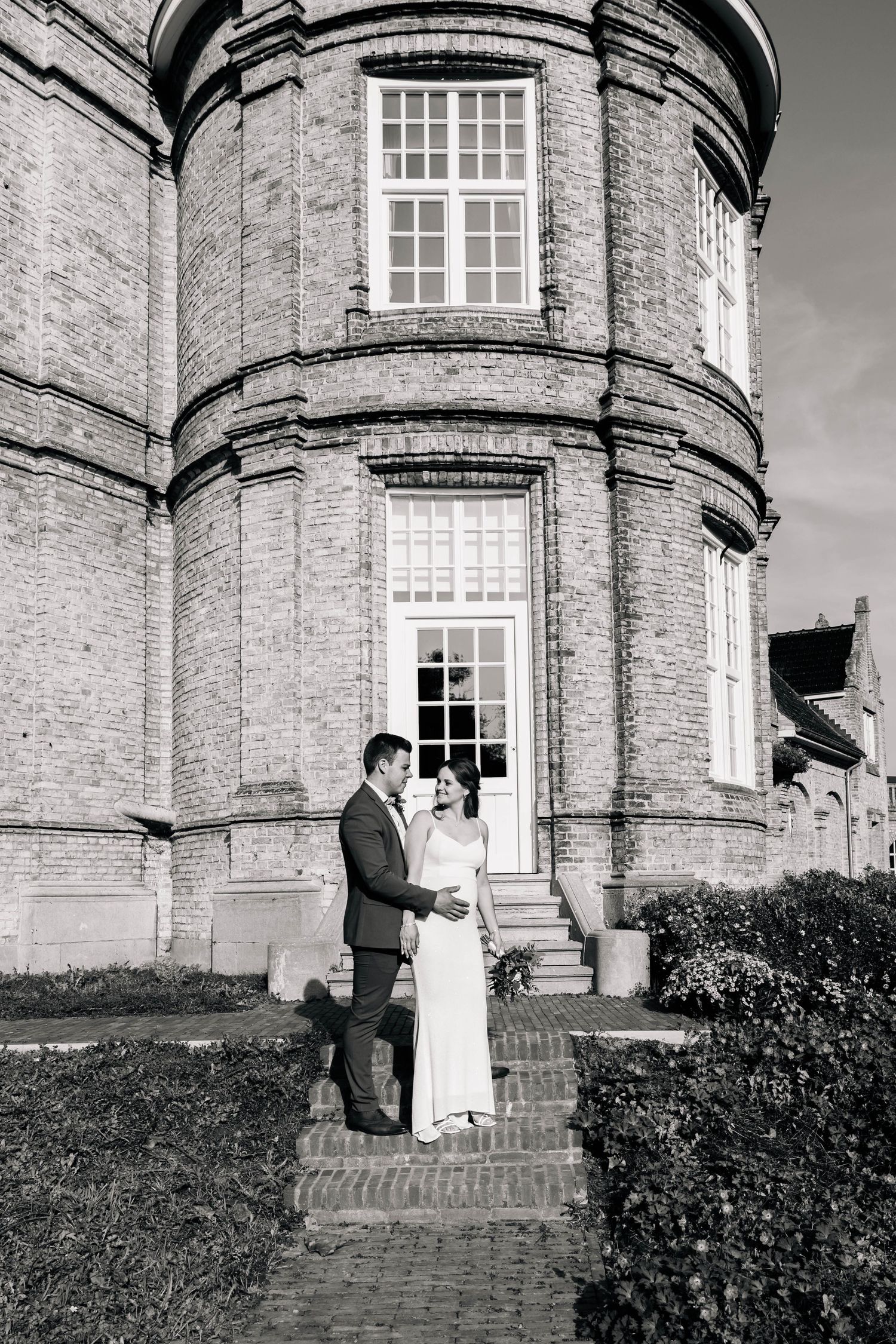 Black and white wedding portrait in front of historic circular brick tower.