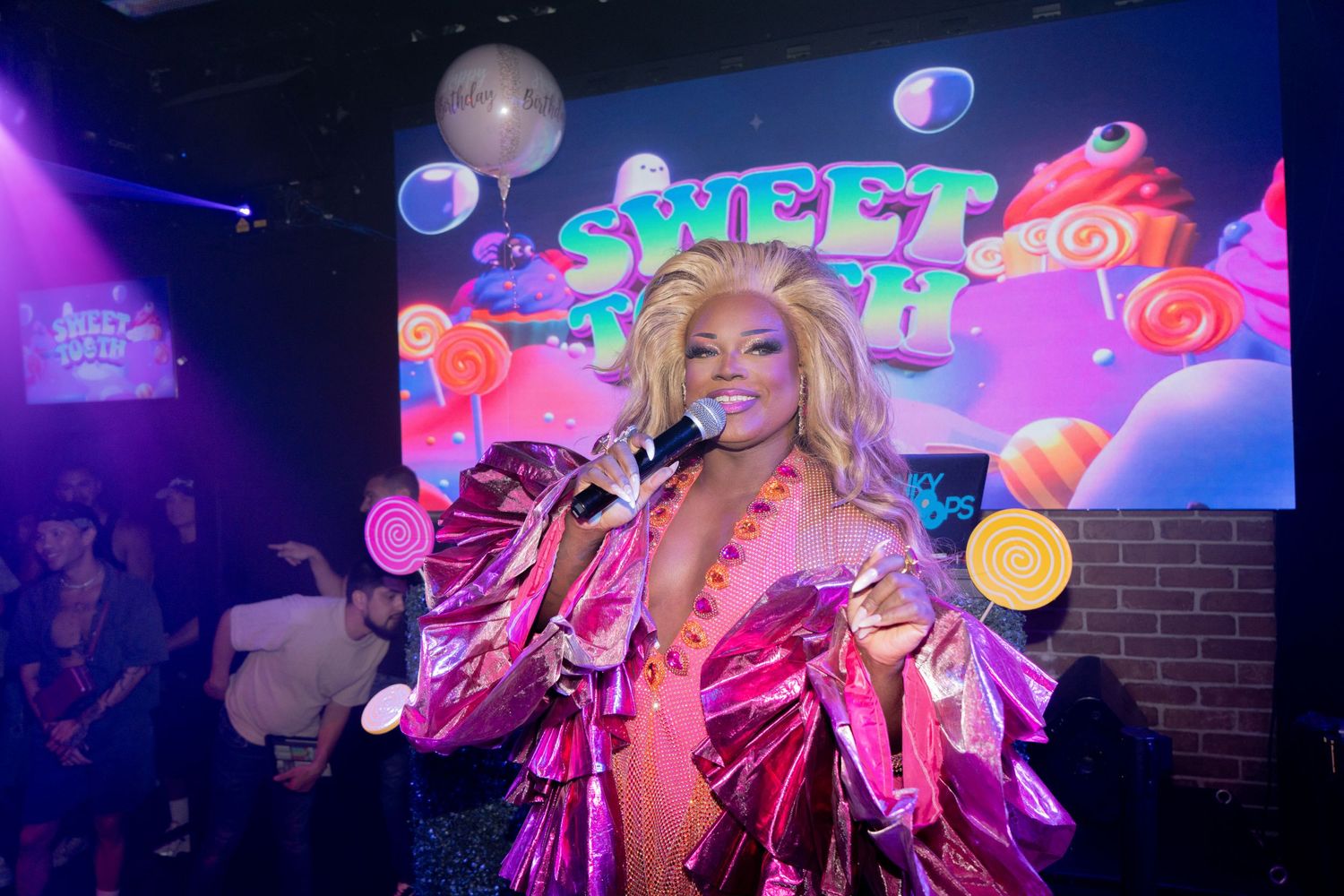 RuPaul Drag Queen Mayhem Miller performs in a ruffled, pink and orange bedazzled costume and looks out into the crowd