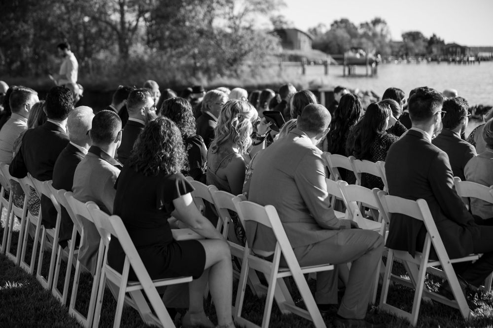 Black and white photo of wedding guests seated in white chairs at an outdoor ceremony.