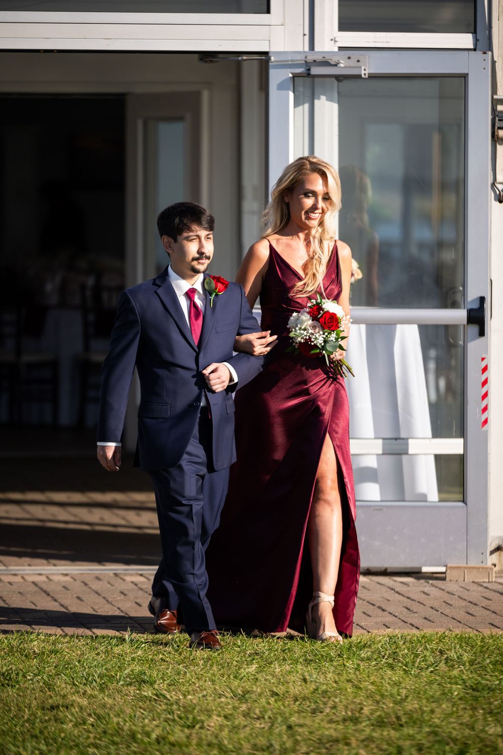 Wedding attendants in formal attire walk together during a sunny outdoor ceremony procession.