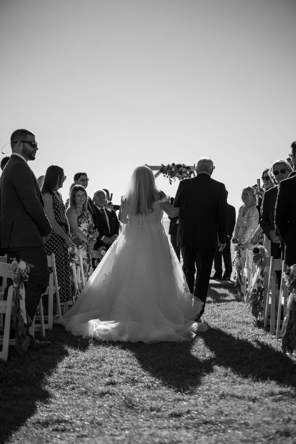 Black and white shot of wedding ceremony guests seated on lawn during outdoor service.