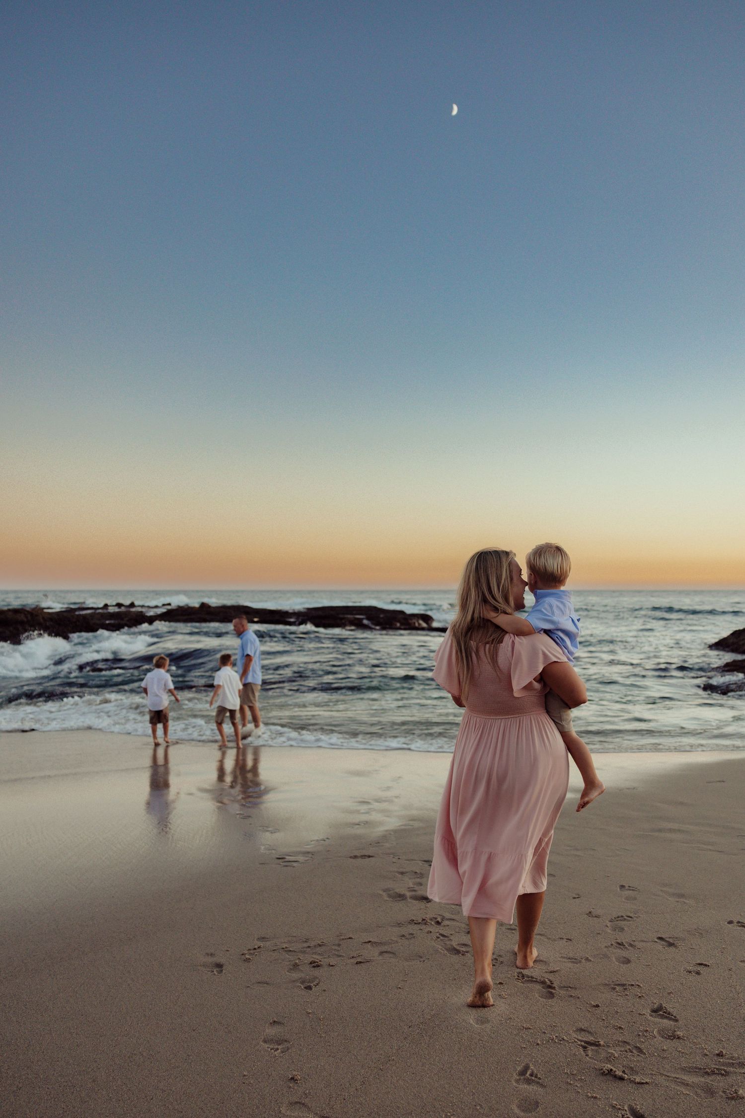 Family walking together hand in hand on a beach during sunset in coordinated blue and white outfits.