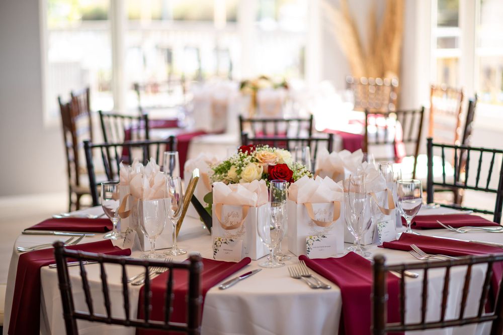 Wedding table settings with burgundy napkins, white favor boxes and crystal stemware.