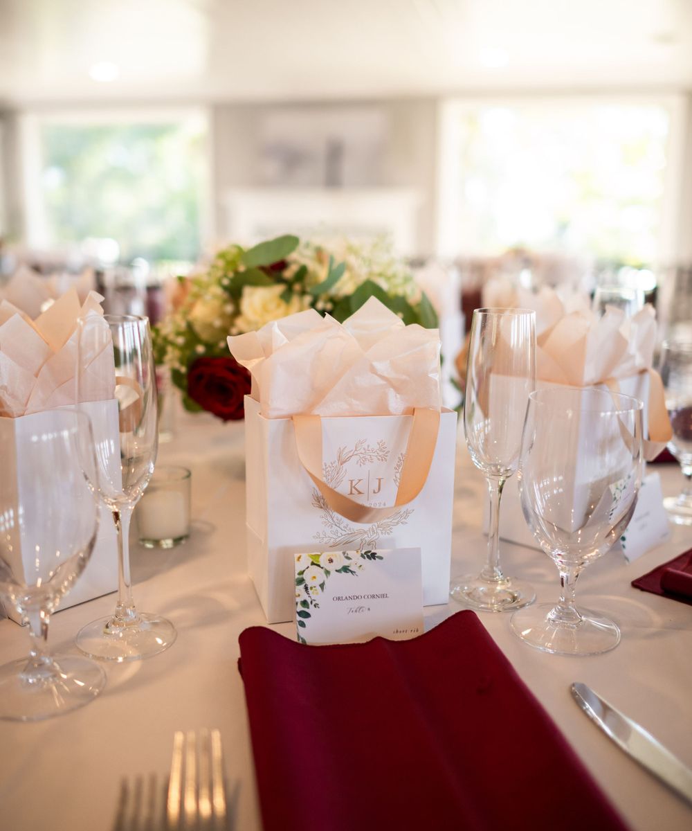 Elegant table setting with burgundy napkins, champagne glasses and white favor boxes.