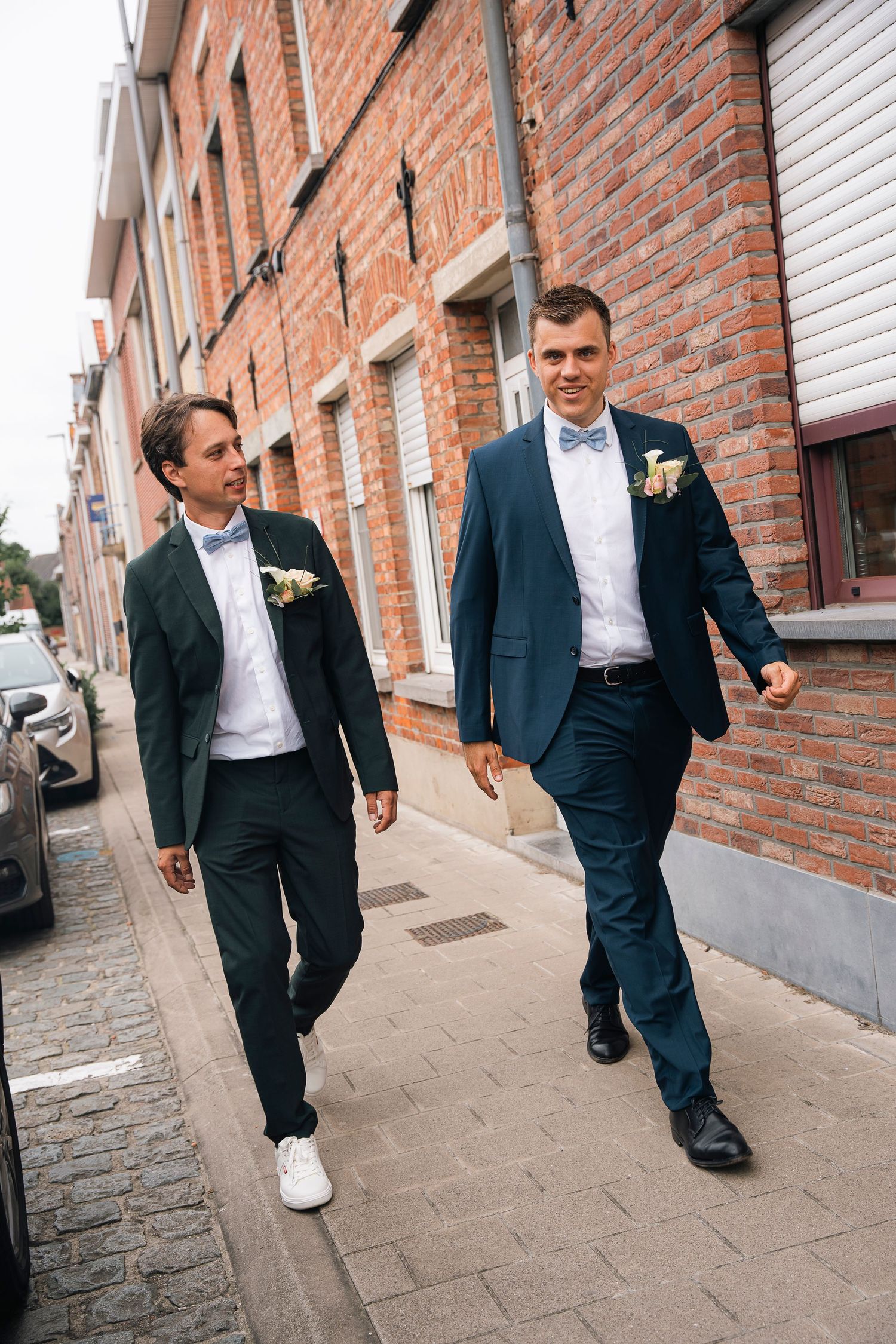Well-dressed wedding couple walking down a cobblestone street with brick buildings.