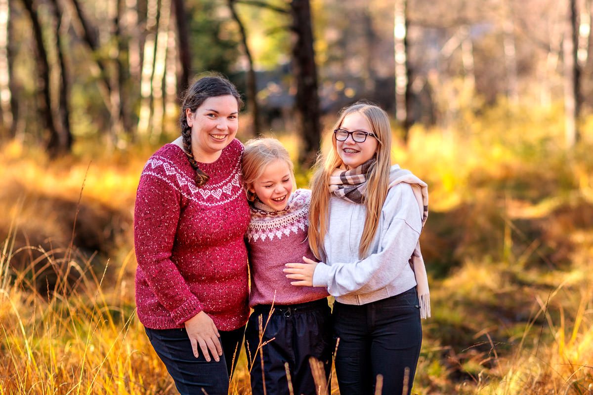 Mor og to døtre står sammen og ler i en solfylt skog på Naglestad i høstfarger.