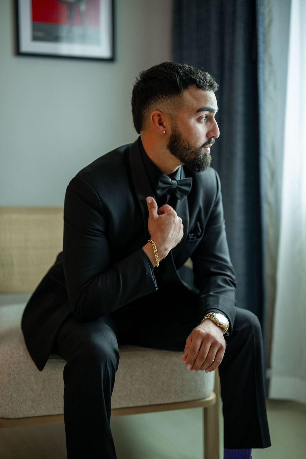 Wedding day portraits showing person in black suit sitting thoughtfully near window.