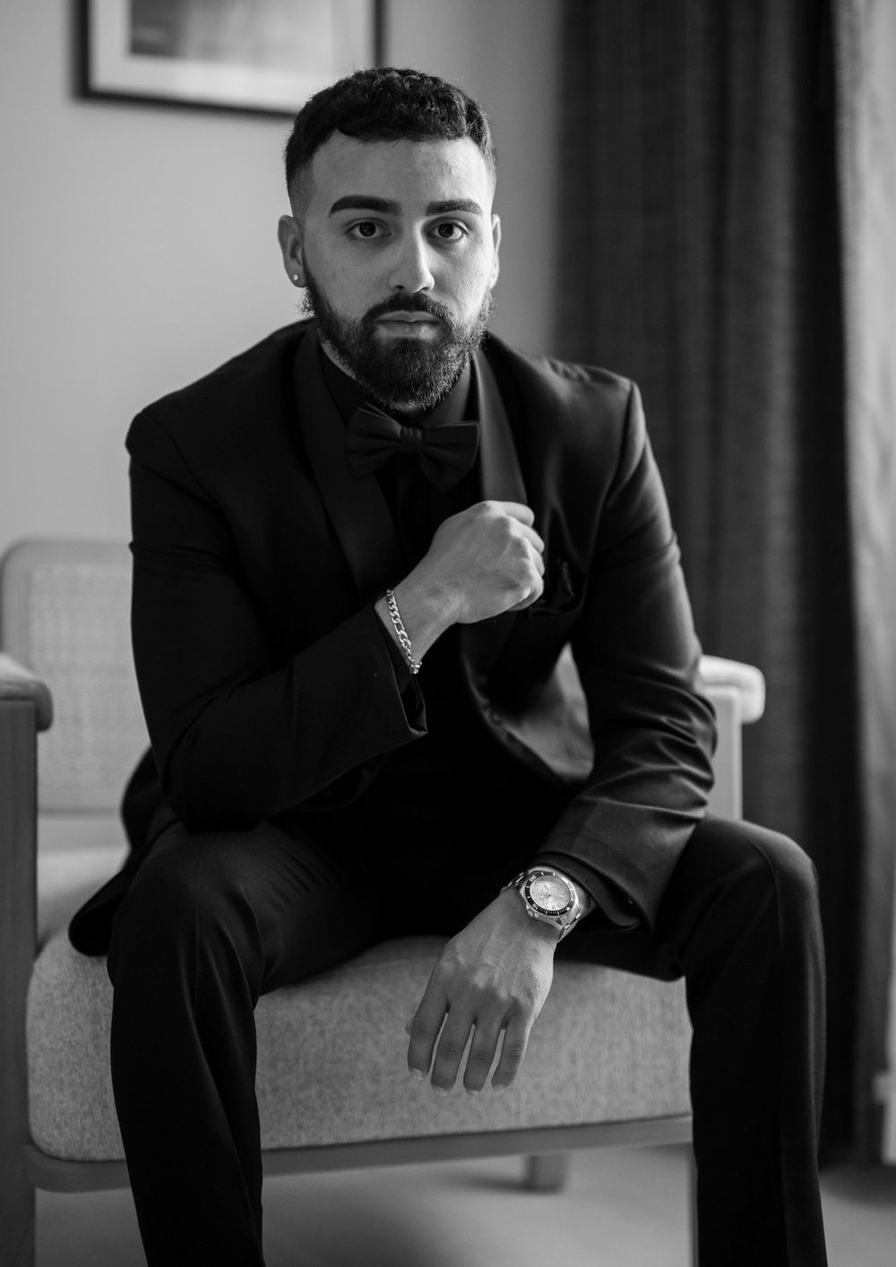 Thoughtful person in black suit sitting on chair in dramatic black and white portrait series.