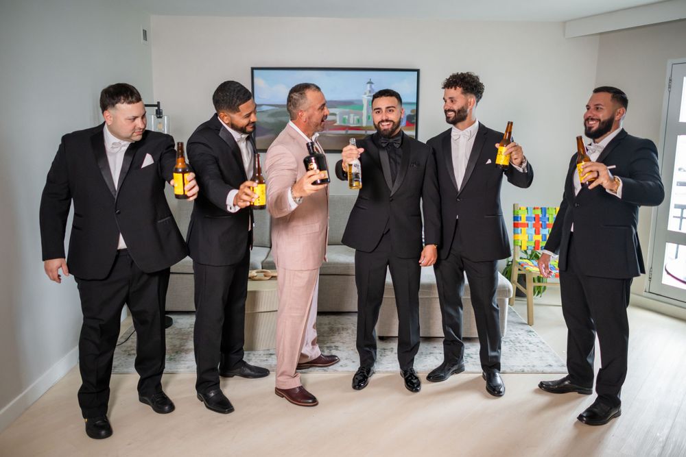 Wedding party in formal attire gathering for group photos in bright indoor space.