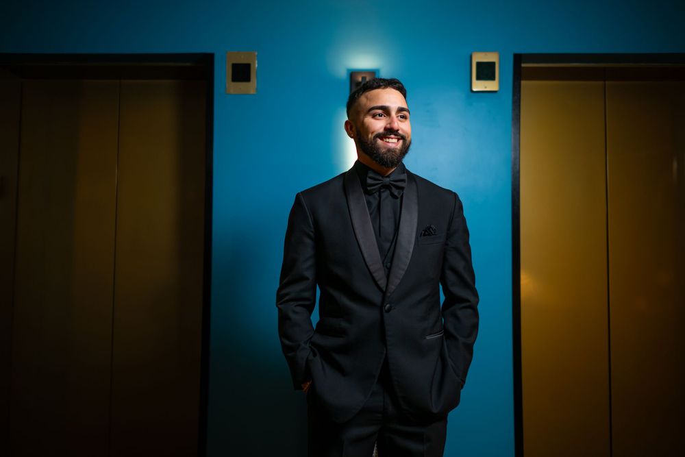 Dramatic portrait against blue wall showing person in formal black attire.