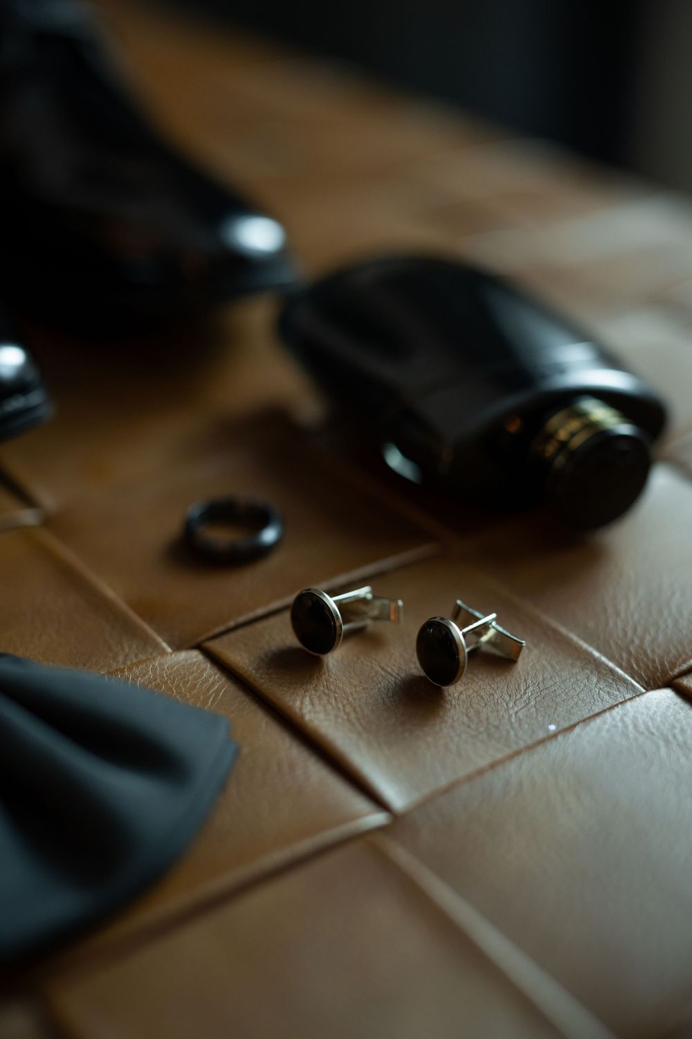 Close-up of black cufflinks and accessories on brown leather surface.