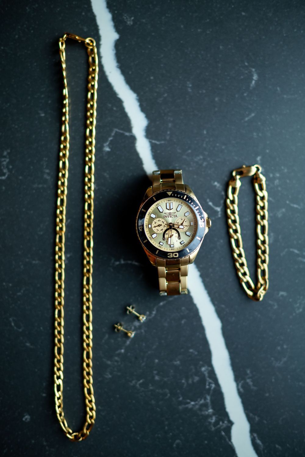 Gold watch and chain accessories displayed on dark marble surface.