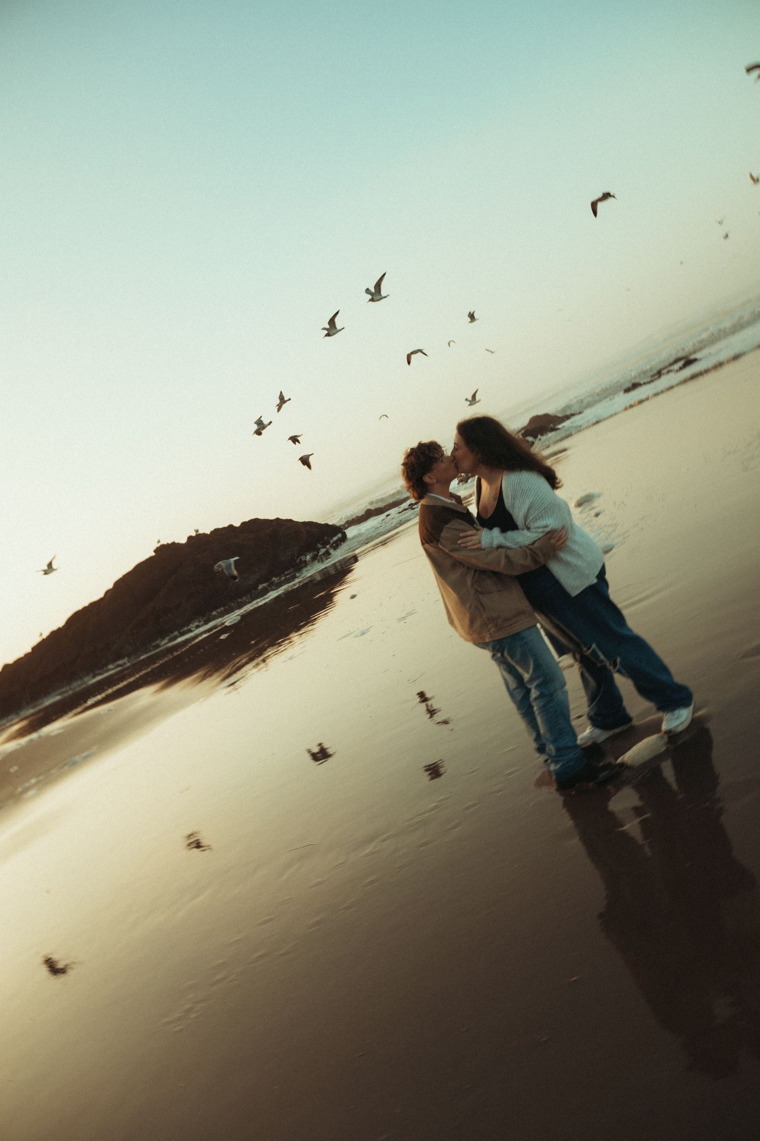Two people wearing straw hats share a tender moment near ocean cliffs on a sunny summer day.