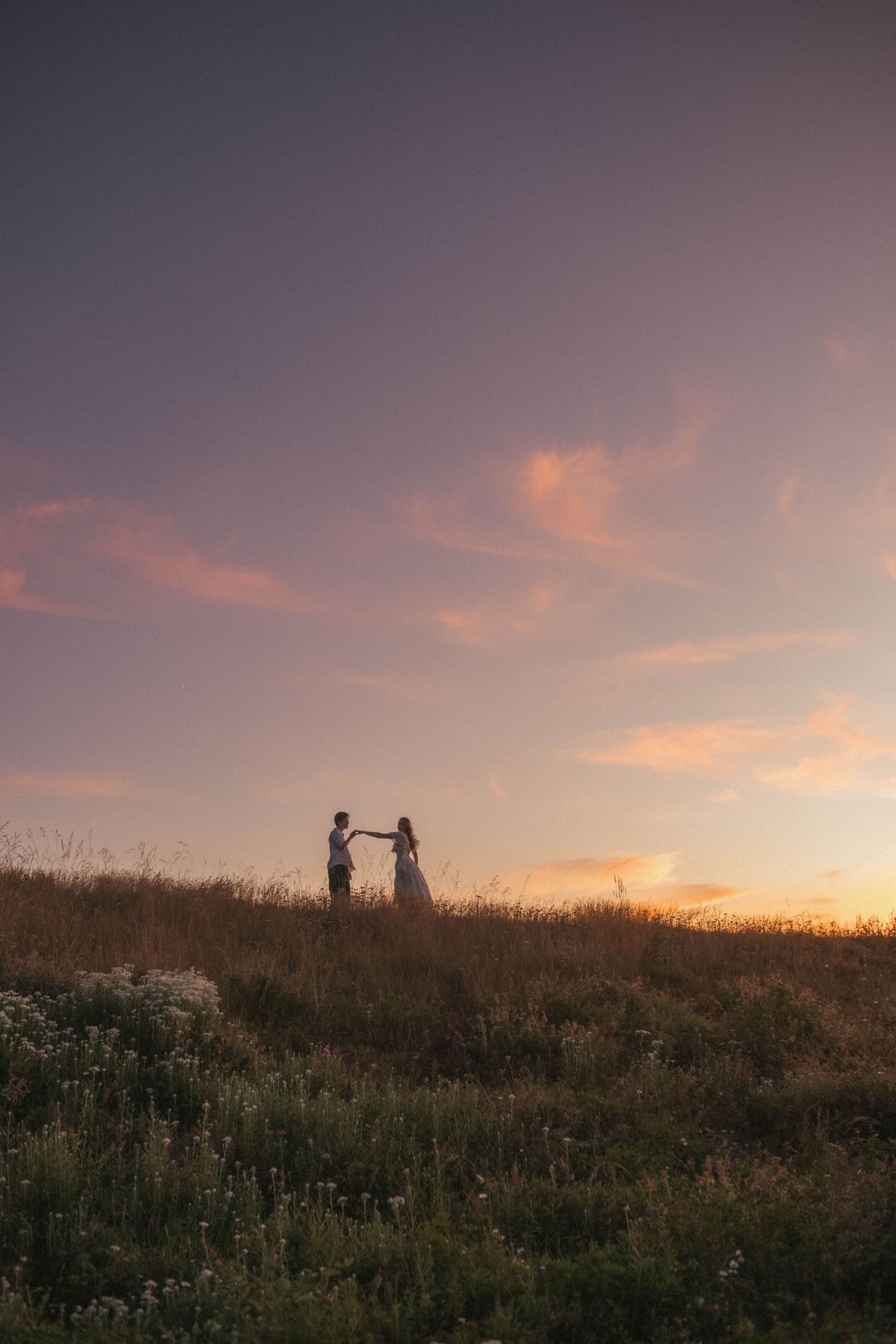Two people wearing straw hats share a tender moment near ocean cliffs on a sunny summer day.