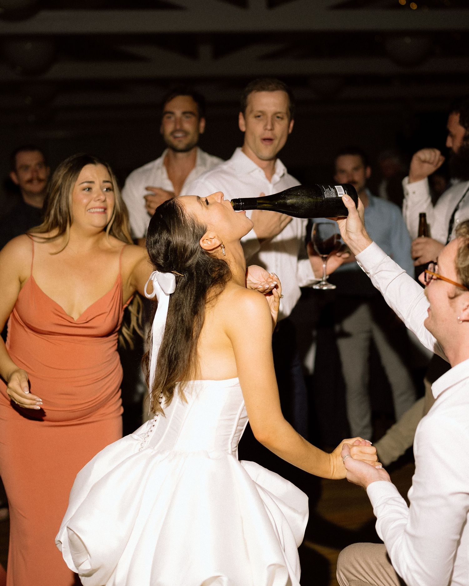 Wedding reception dance party with guests in coral dresses and white attire.