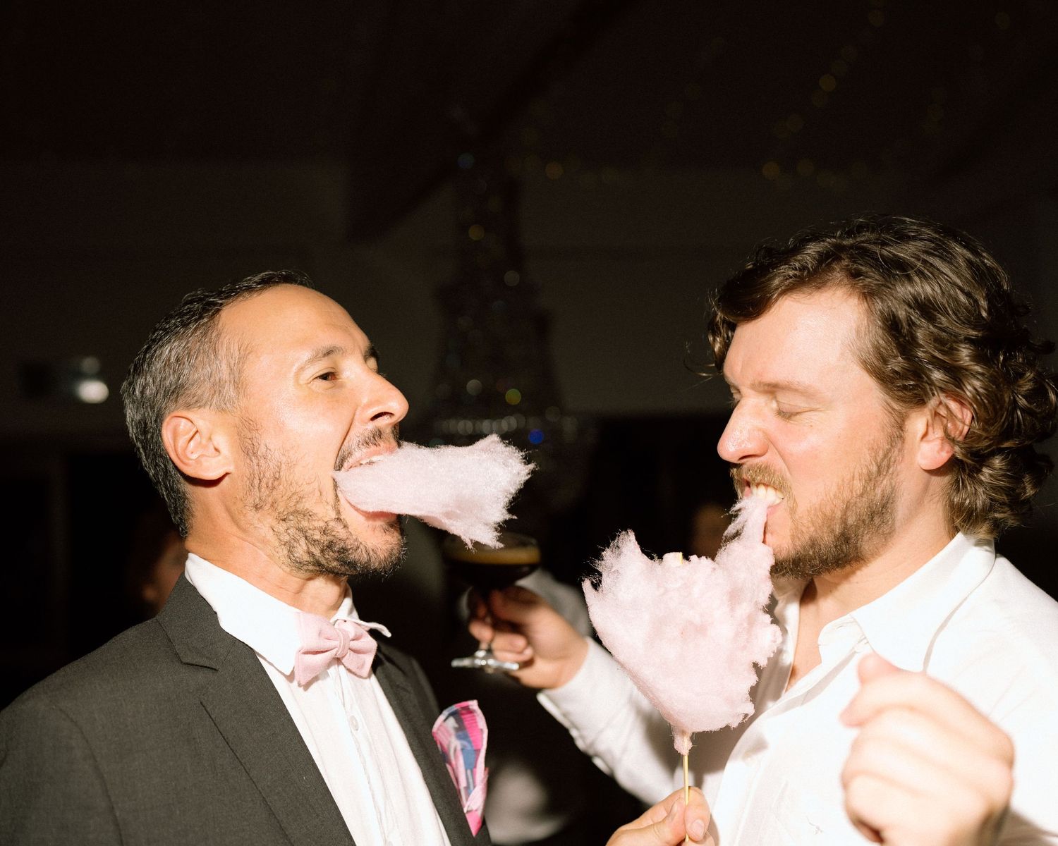Two wedding guests laughing and celebrating with cotton candy at reception.