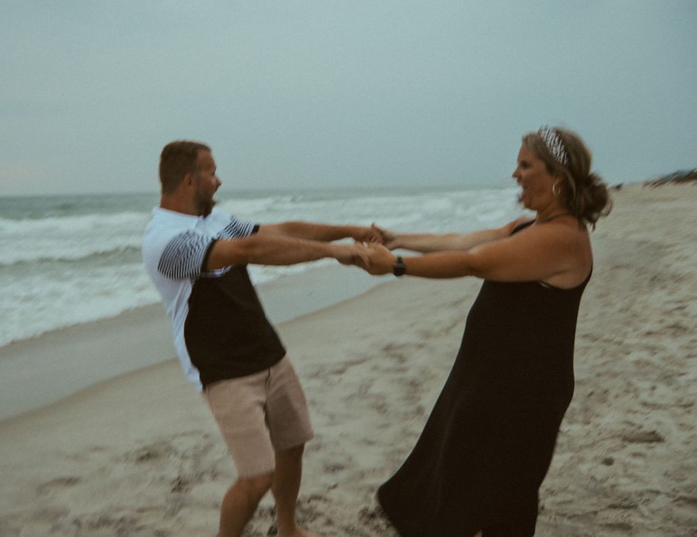 couple twirling each other around on the beach for a photo session