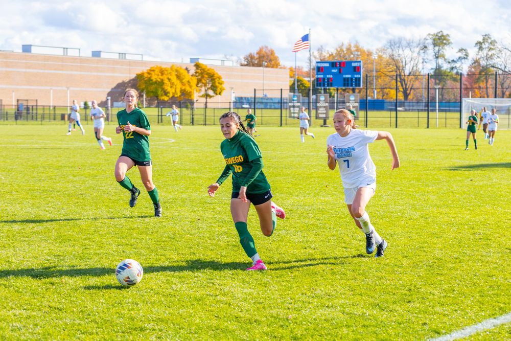 Soccer players chase after the ball during an intense match on a sunny grass field.