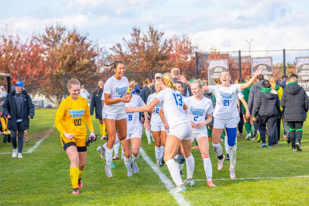 Soccer players in white and yellow uniforms running together across a grass field during a team warmup drill.