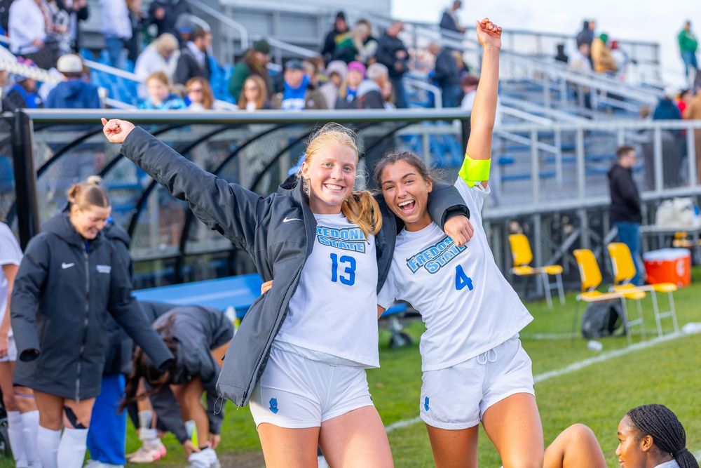 Soccer players in blue and white uniforms celebrating together near the sideline during a match.