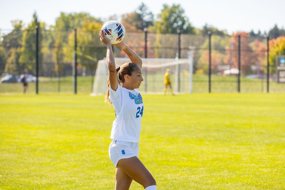 Soccer player in white jersey throws the ball in during a sunny autumn match on a grass field.