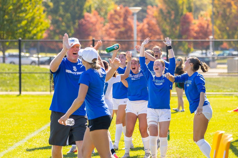 Rugby players in blue and white uniforms celebrate together on a sunny field during a match.