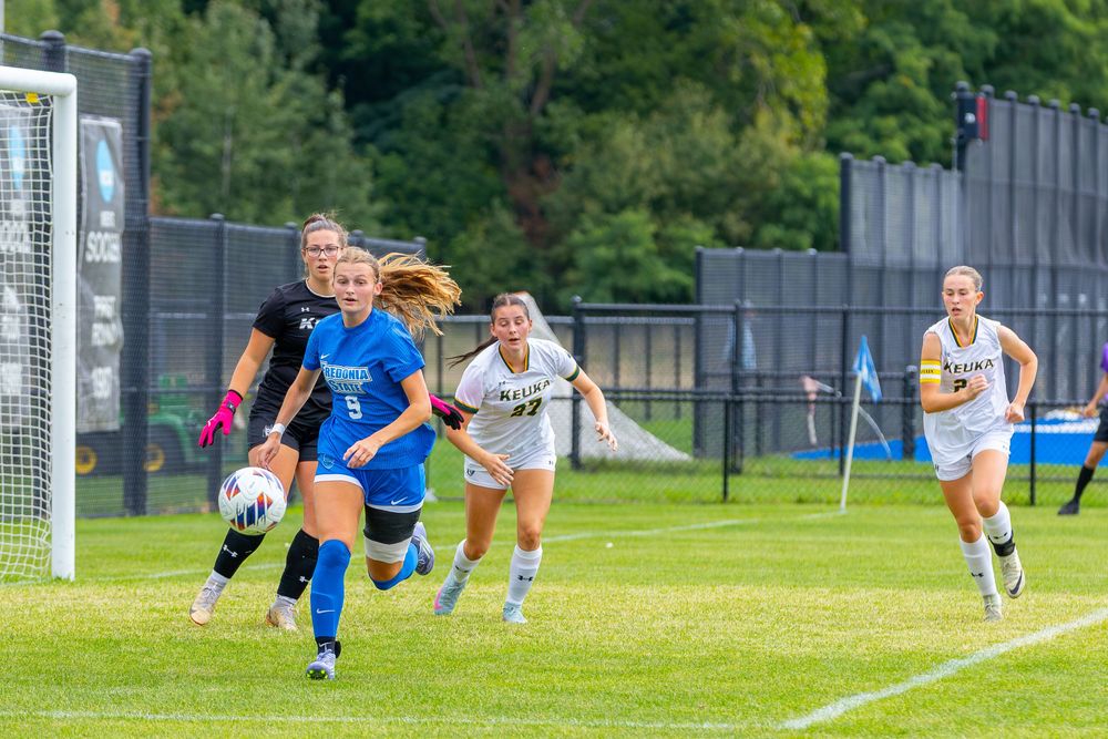 Soccer players dive and stretch on a grass field during an intense match near the goal area.