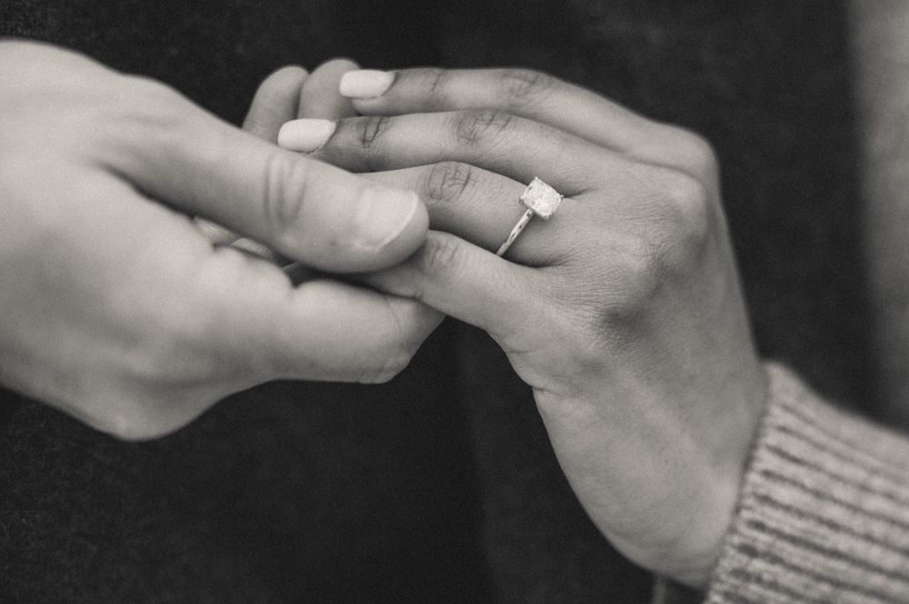 Close-up black and white shot of hands exchanging wedding rings.