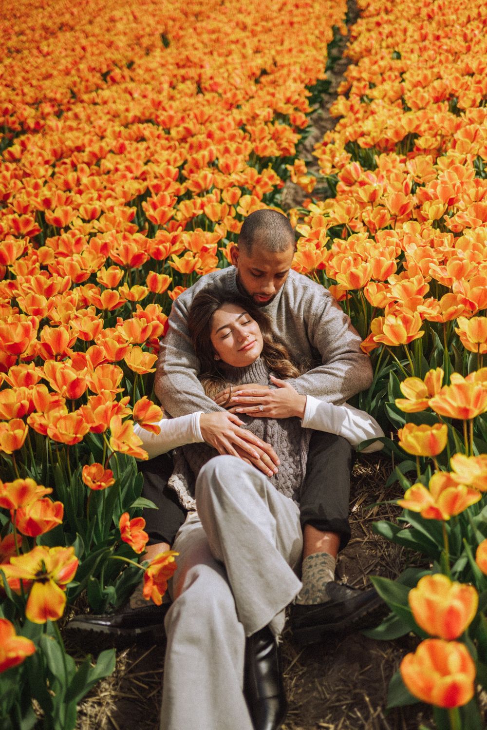 Couple lying among bright orange tulips in a Dutch flower field during spring.