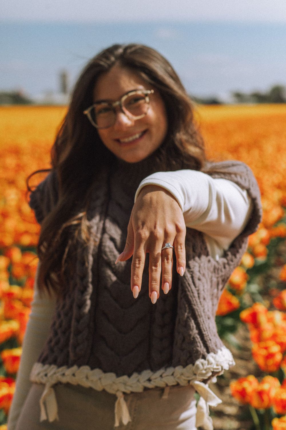 Close-up of hands showing off engagement ring against vibrant orange tulip field background.