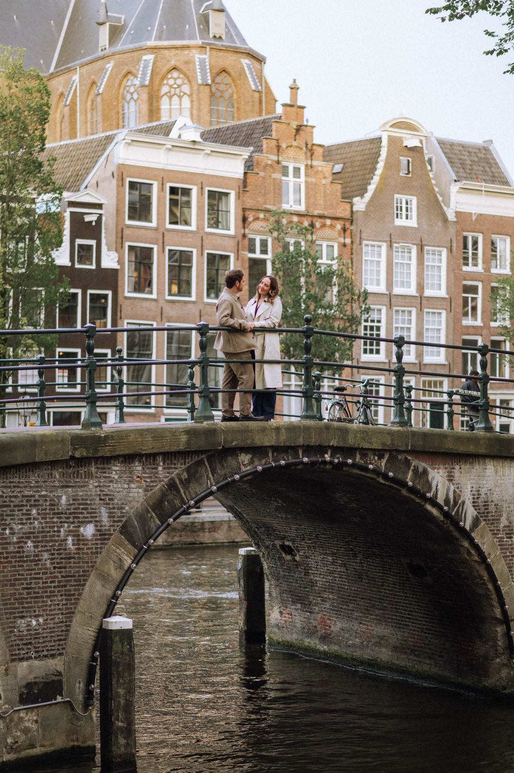 Romantic scene on a canal bridge in Amsterdam with traditional Dutch architecture in the background.