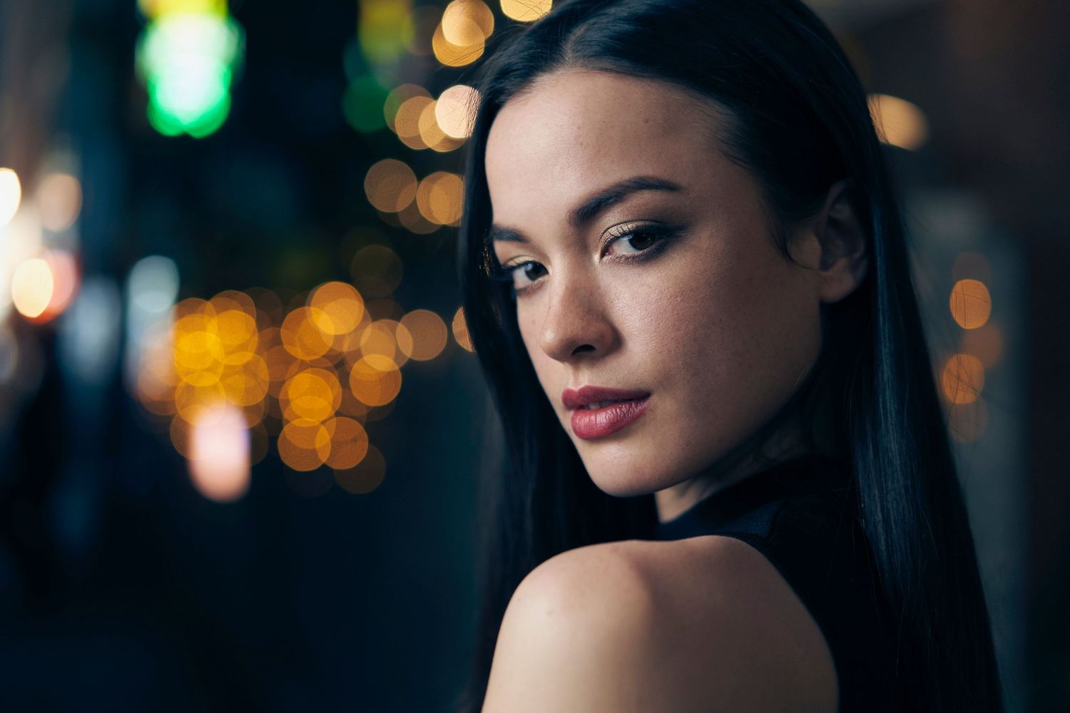 A portrait at night with soft bokeh lights in the background creating an exciting, moody urban atmosphere