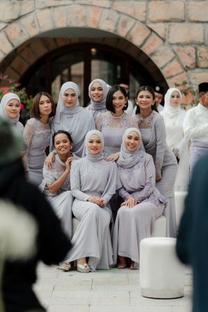 Bridal party in coordinated grey and lavender outfits posed in front of stone archway.